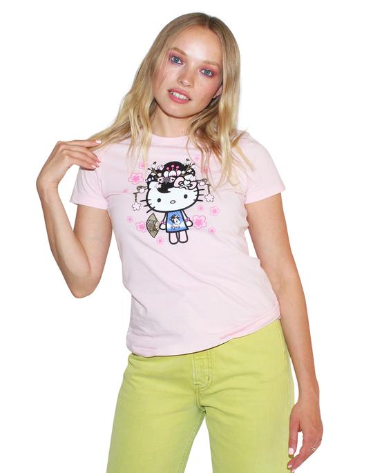 A woman wearing a pink t-shirt with Hello Kitty and a tokidoki logo on the upper back, paired with green pants.